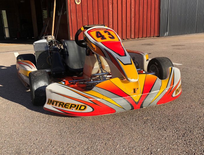 Go-kart med nummer 43 parkerad på asfalt framför en röd lada.