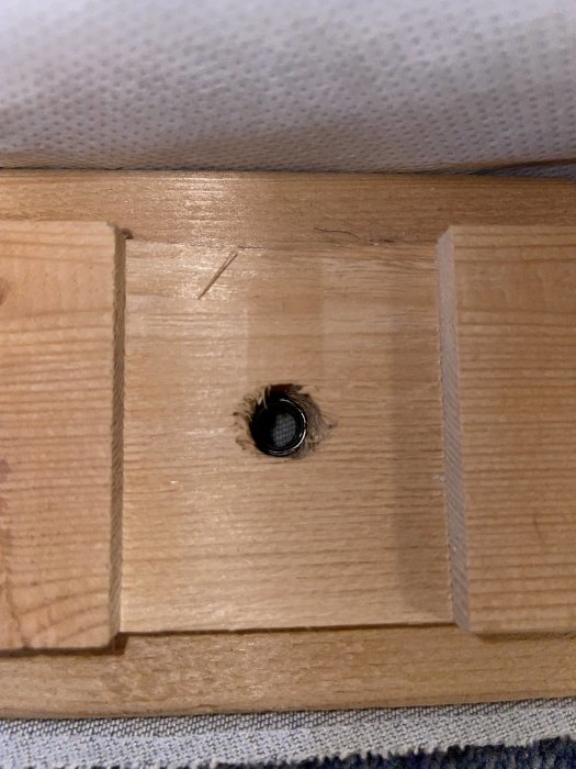 Närbild på ett hål i en trädel av en säng med en synlig gänga inuti hålet.