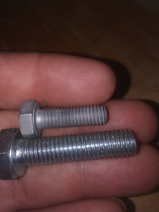 Två metallbultar av typen M8 och M10 som hålls i en hand.