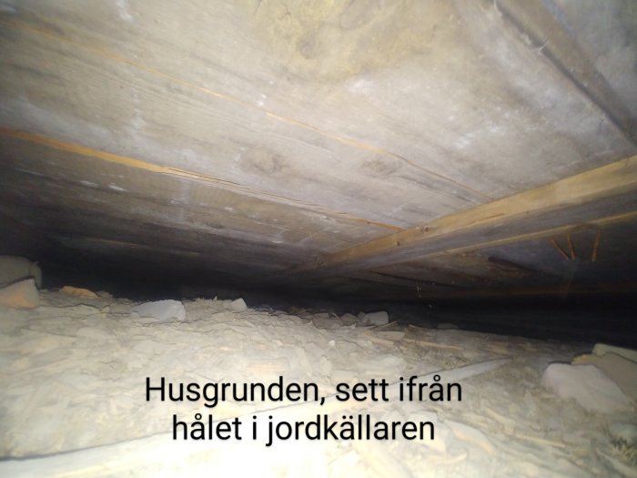 Låg krypgrund under hus, synlig från hål i jordkällare, mögel och fuktindikationer.