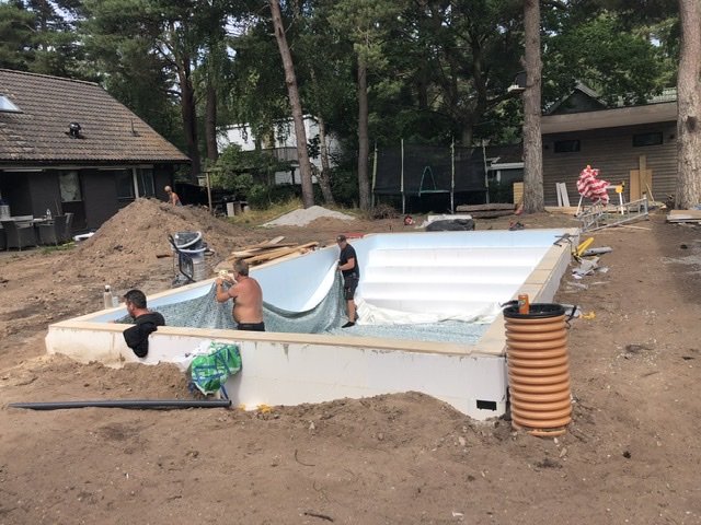 Installation av pool med liner och slangar på en byggarbetsplats med arbetare och byggmaterial.