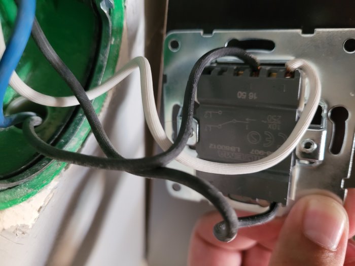 Installation av eluttag med synliga elektriska kablar och en hand som håller i uttaget.