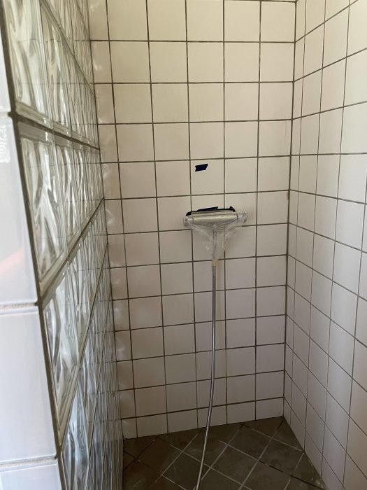 Nyfogad duschdel med vita kakelväggar och glasblocksvägg, duschslang och blandare syns.