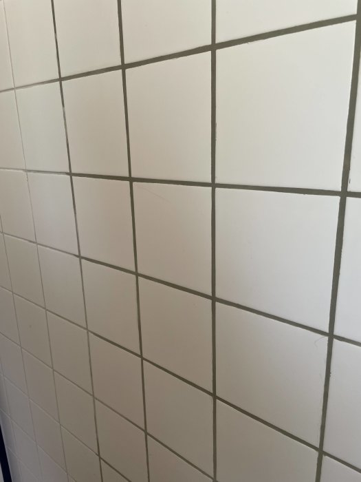 Nyligen omfogade vita badrumskakel med färska fogar och en synlig spricka i en kakelplatta.