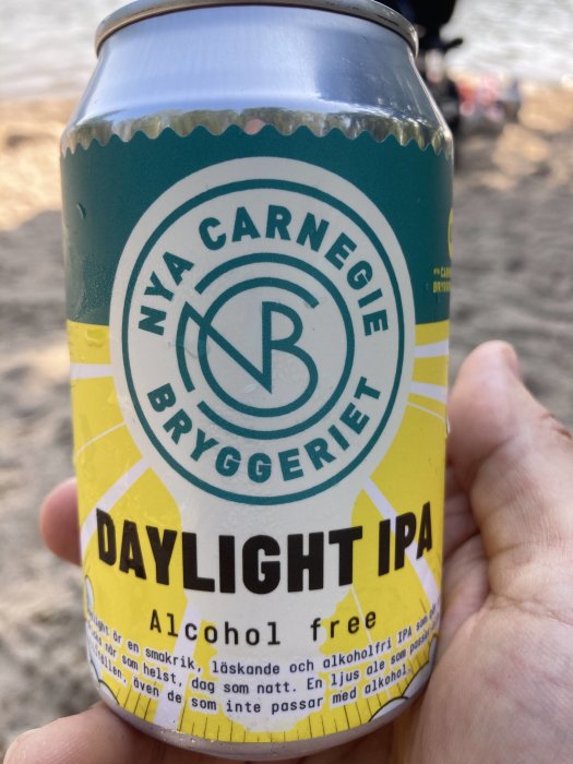 Hand håller en burk Nya Carnegiebryggeriet Daylight IPA alkoholfri öl på stranden.