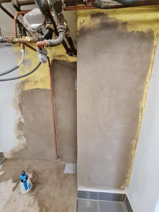 Nyputsad vägg och hörn i ett renoveringsprojekt med synliga rör och installationsdelar.
