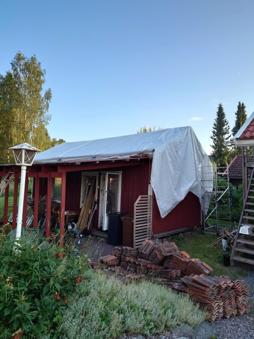 Renoveringsprojekt av ett uthus med borttagna takpannor och presenning över taket.