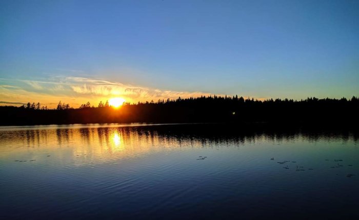 Solnedgång över Ölsjön med skogssiluett i Ramsberg, spegling i vattenytan.