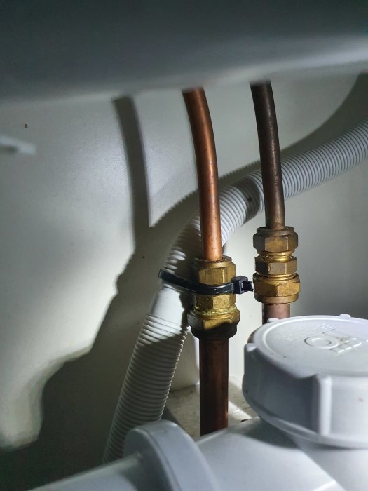 Kopparledningar och ventiler under köksbänk, saknar synlig avstängningsventil.