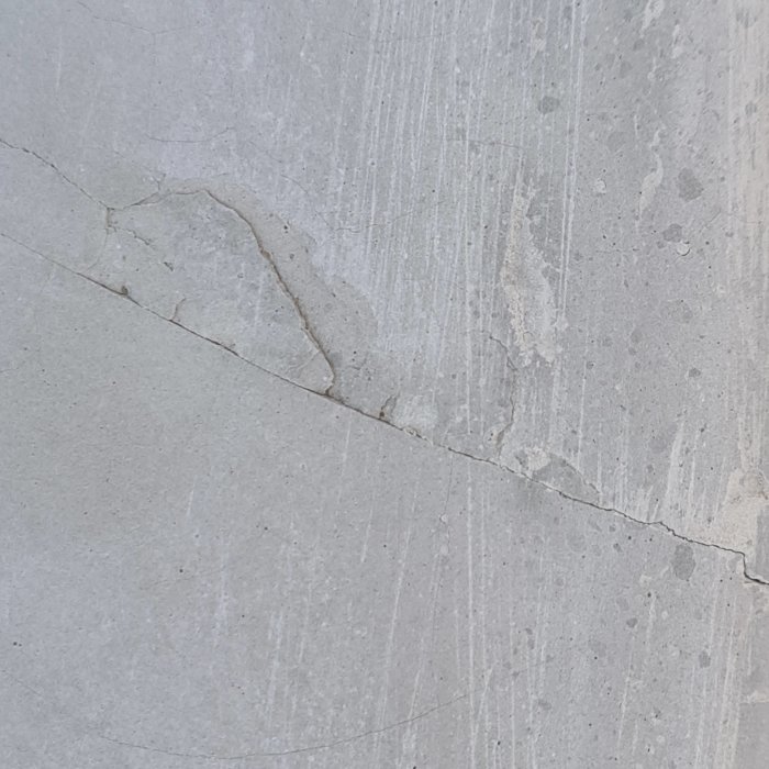 Egengjuten betongskiva med små och stora torrsprickor samt några områden där betongen är porös och flagnad.