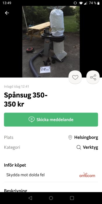 En spånsug anordning med svart slang och vit påse står utomhus framför en bänk och grönt gräs.