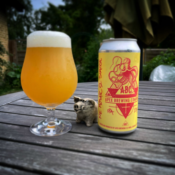 Ölglas med skummande dryck och en burk bredvid en liten grisfigur på ett träbord.