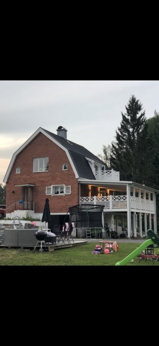 Tvåvånings tegelhus med vit altan och möjlighet för tillbyggnad längs altanens sida.