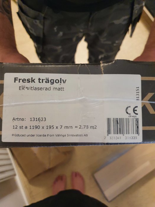Etikett på förpackning av 'Fresh trägolv' med specifikationer, i en inomhusmiljö, synliga fötter och en person stående.