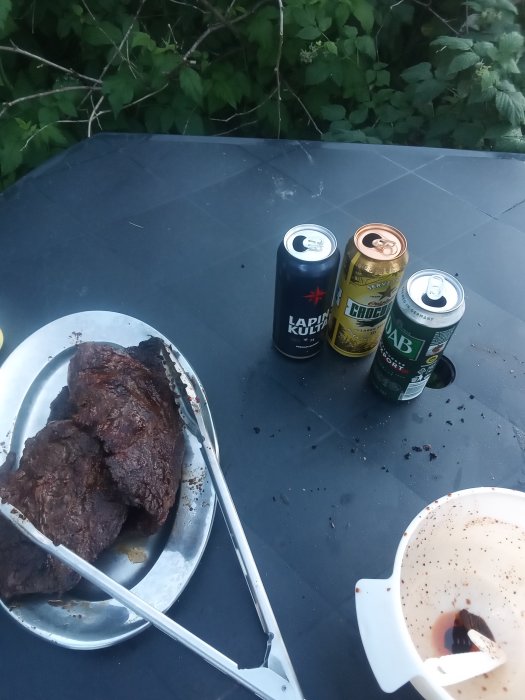 Grillade kycklingspett och tre ölburkar på ett bord, tycks vara en avslappnad grillkväll.