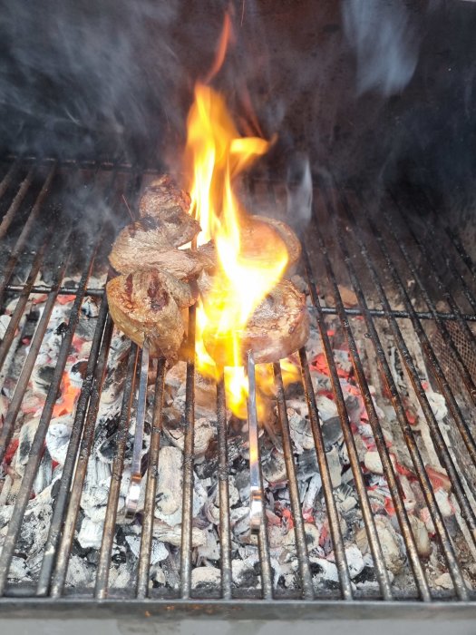 Picanha-stekar på grill med lågor från fett som antänts, glödande kol nedanför.