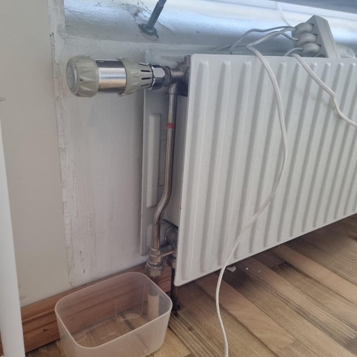 Läckage vid AGA termostat på radiator, rörkoppling märkt AHA med röd tejp, skål under för att samla upp vatten.