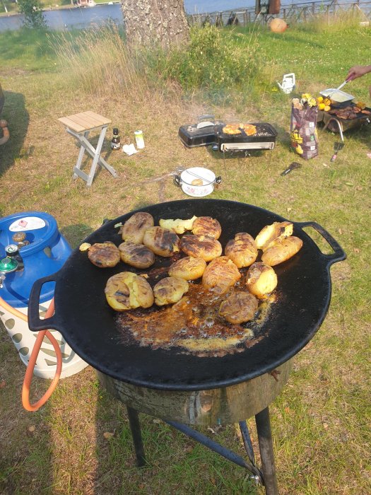 Grillning av potatishalvor på muurikka utomhus, med en husvagnscampings miljö i bakgrunden.