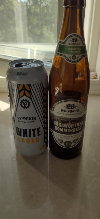 En burk Pyynikin White Lager och en flaska Wieninger Höglworth Sommierbier mot ett fönster.