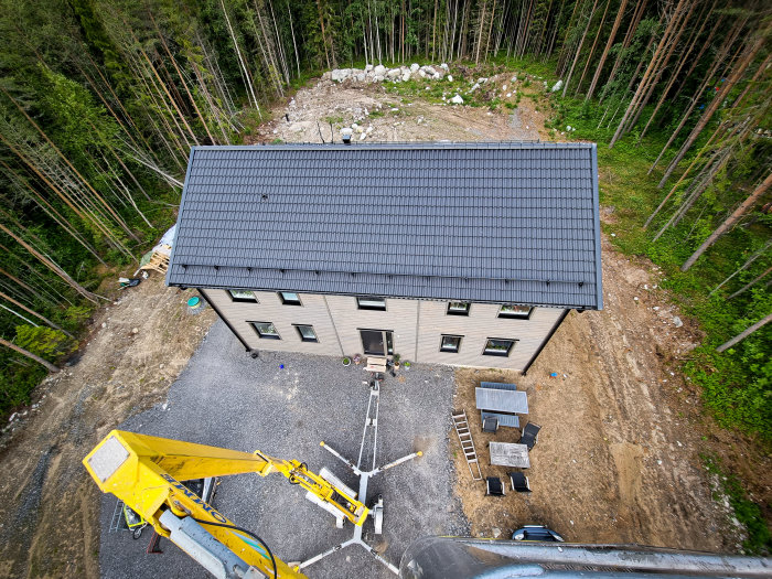 Vy ovanifrån av ett hus med nymålad ljus fasad och mörkt tak, skylift nära huset i en skogsmiljö.