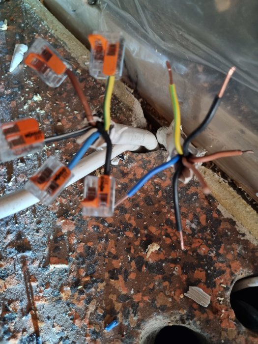 El-installation med färgkodade elkablar och kopplingsklämmor på ett granitgolv, felaktigt kopplade orsakar strömbrytning.