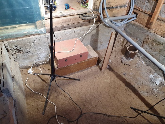 Renoverat badrum med uppbilat betonggolv och synlig sand, avloppsrör och byggmaterial.