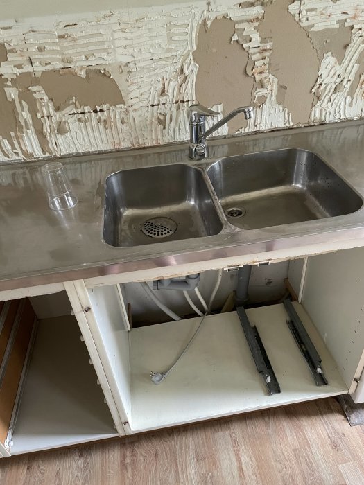 Köksdiskbänk med avlägsnad inredning och synliga VVS-installerade rör under.