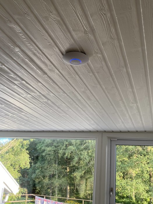 Unify Lite 6 accesspunkt installerad i taket i ett rum med trädetaljer och utsikt genom fönster.