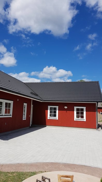 Ny lagd naturgrå tumlad marksten från St Eriks med antracitkanter framför rött hus.