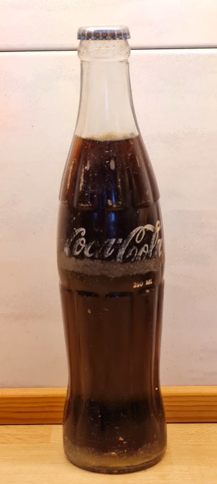 Klassisk långsmal Coca-Cola glasflaska från Tanzania 1985 på en bänk.