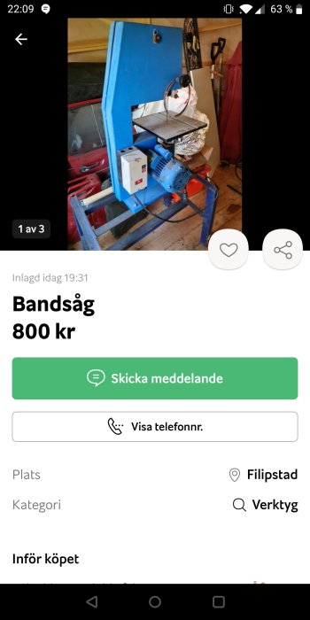 Blå stående bandsåg i ett verkstadsutrymme med diverse verktyg i bakgrunden.