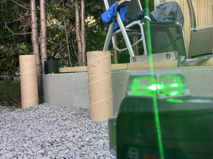 Betongplatta med laserlinje som visar höjdskillnader bredvid husfasad och grus.