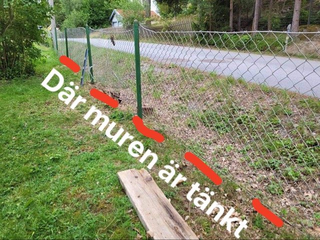 Suttande tomtmark med textmarkeringar för planerad mur, staket vid väg och omgivande vegetation.