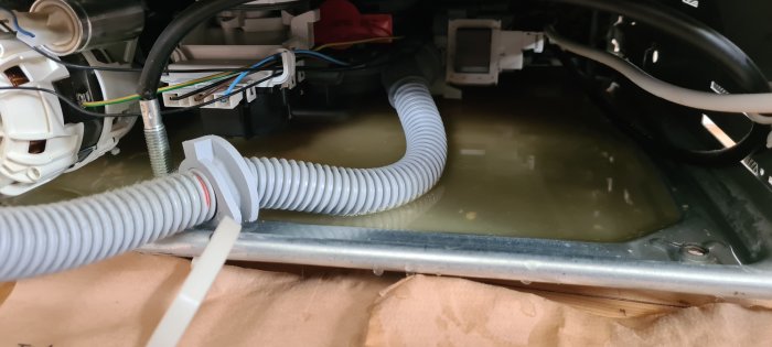 Vattenansamling på bottenplattan av en apparat med synliga sladdar och komponenter.