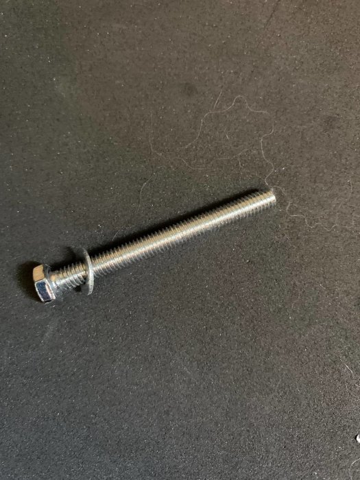 En lång metallskruv med delvis gängad skaft och en mutter på en svart bakgrund.