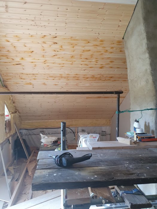 Renoveringsplats med pärlspont i taket, oisolerade väggar och verktyg på arbetsbänk inför trapphålstagning.