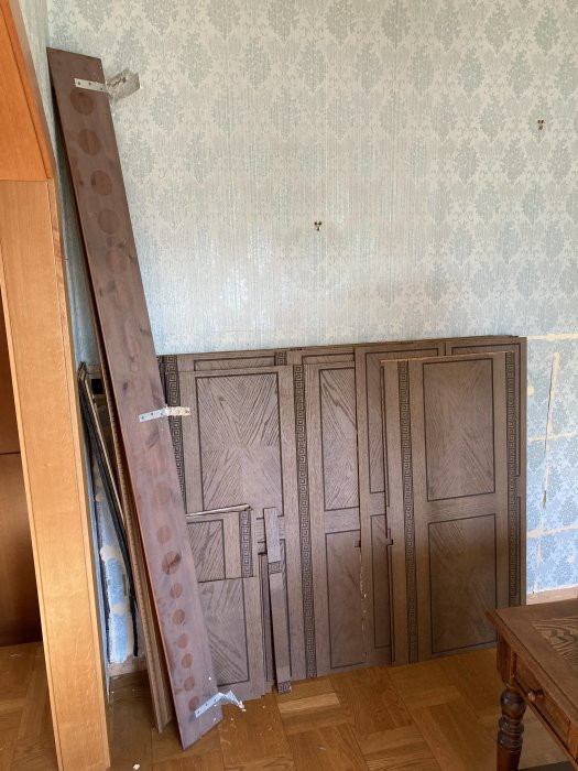 Nedmonterad brun bröstpanel liggande intill vägg i ett rum med tapeter och parkettgolv.