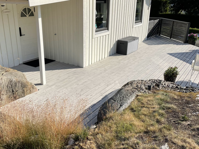 Nymålad ljusgrå altan framför hus med vita väggar och svart dörr.