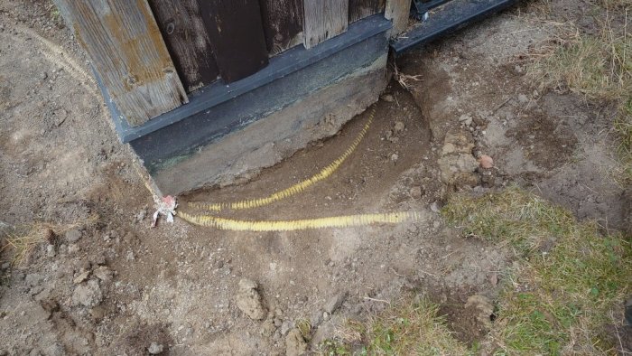 Grävd mark med gul markslang som leder el till en byggnad, synlig isolering och jordlager.