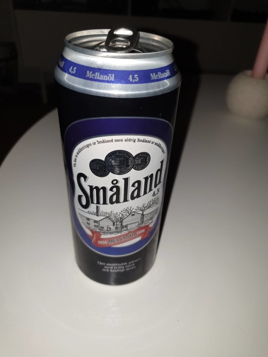 En ölburk märkt "Småland Mellanöl" med 4.5% alkoholhalt på ett vitt bord med svagt bakgrundsljus.