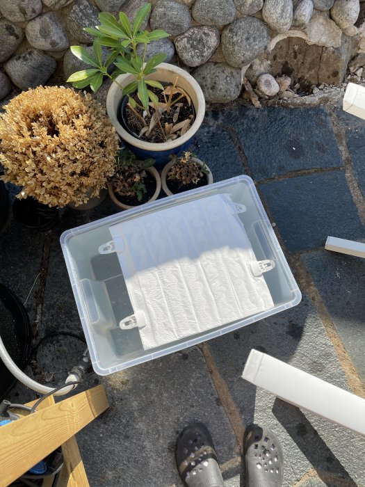 Test av kanalplast inuti en presenning för att skapa ett DIY pooltak, med byggmaterial och växter i bakgrunden.