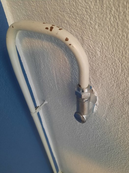 Rostfläckad vattenutkastare fastskruvad på en blå vägg, ifrågasättande om demontering.