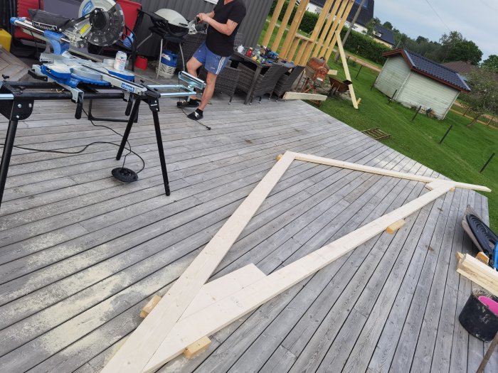 Egenbyggd takstol av trä på en altan med verktyg och en person i bakgrunden som arbetar på ett byggprojekt.