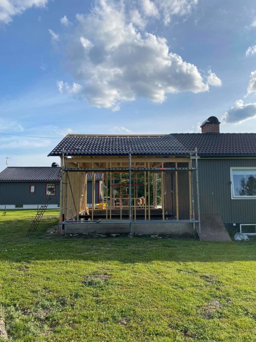 Hus under renovering med nytt tak och takpannor, ställningar runt bygget, grön gräsmatta i förgrunden.