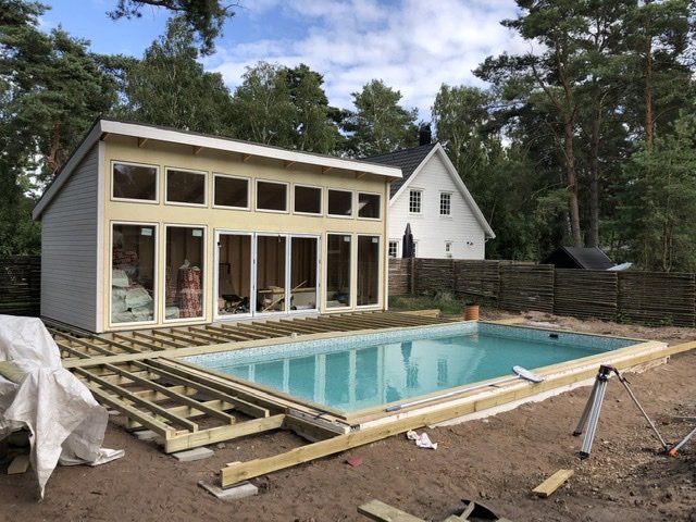 Nytt modernt hus med stora fönster vid konstruktion av trädäck runt en uppfylld pool.