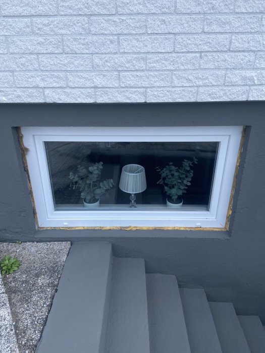 Nyinstallerat fönster på husgrund med lampa och växter på fönsterbrädan.