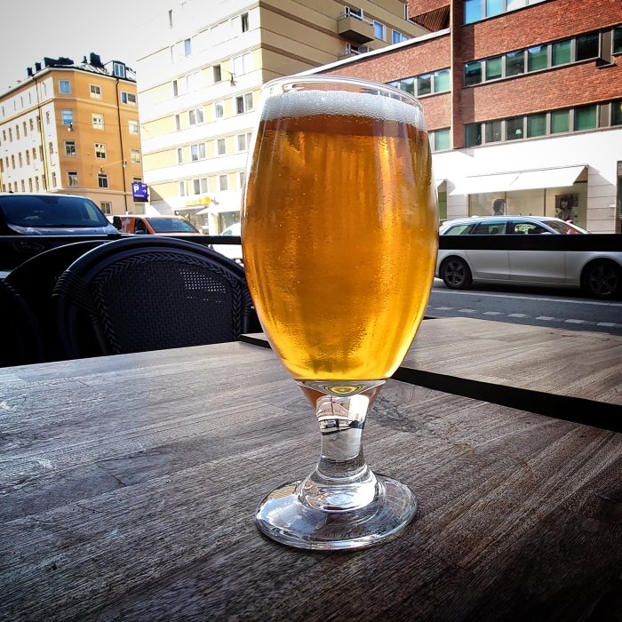 Glas med ljus öl på uteservering av Mackinlays Inn, stadsbakgrund, Stockholm.