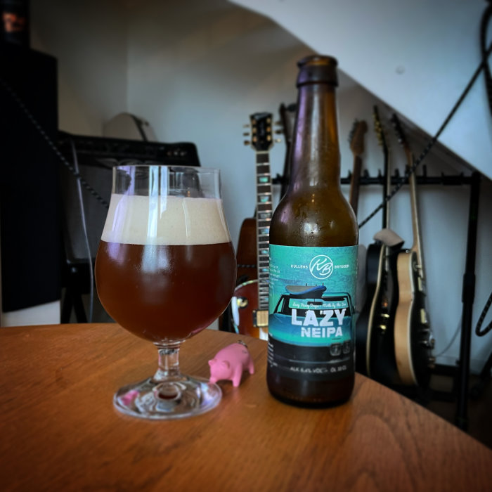 Flaska och glas med öl märkt "LAZY NEIPA", i bakgrunden suddiga gitarrer.