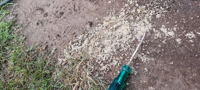 Ett långt kopparrör med sand omkring, delvis nedsänkt i jorden, vid sidan om gräs och jord.