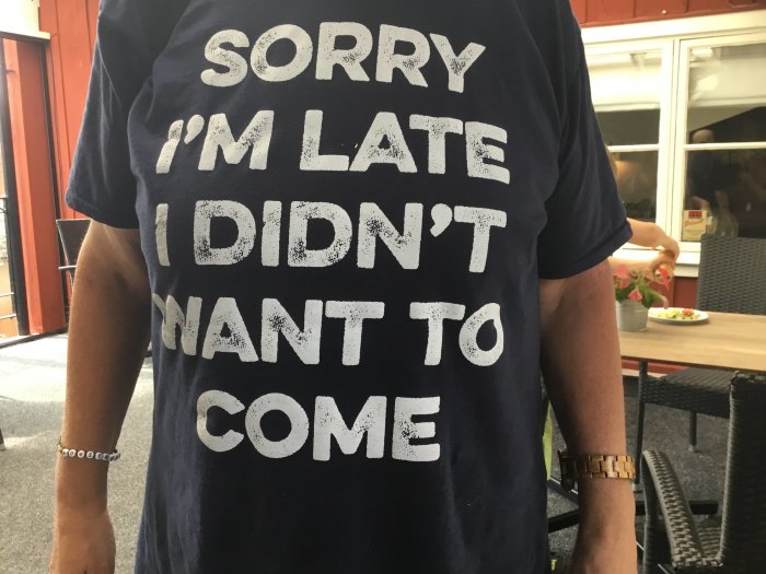 Person med en humoristisk T-shirt där det står "SORRY I'M LATE I DIDN'T WANT TO COME